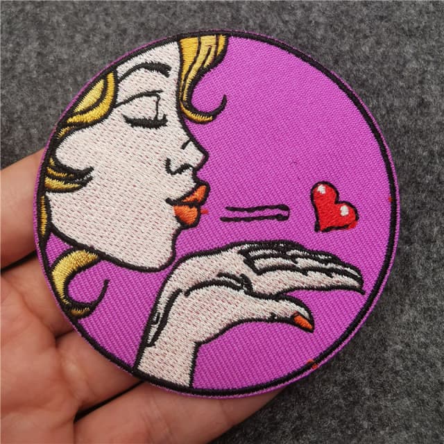Round woven patch with a pop-art woman blowing a kiss and a red heart, held in a hand
