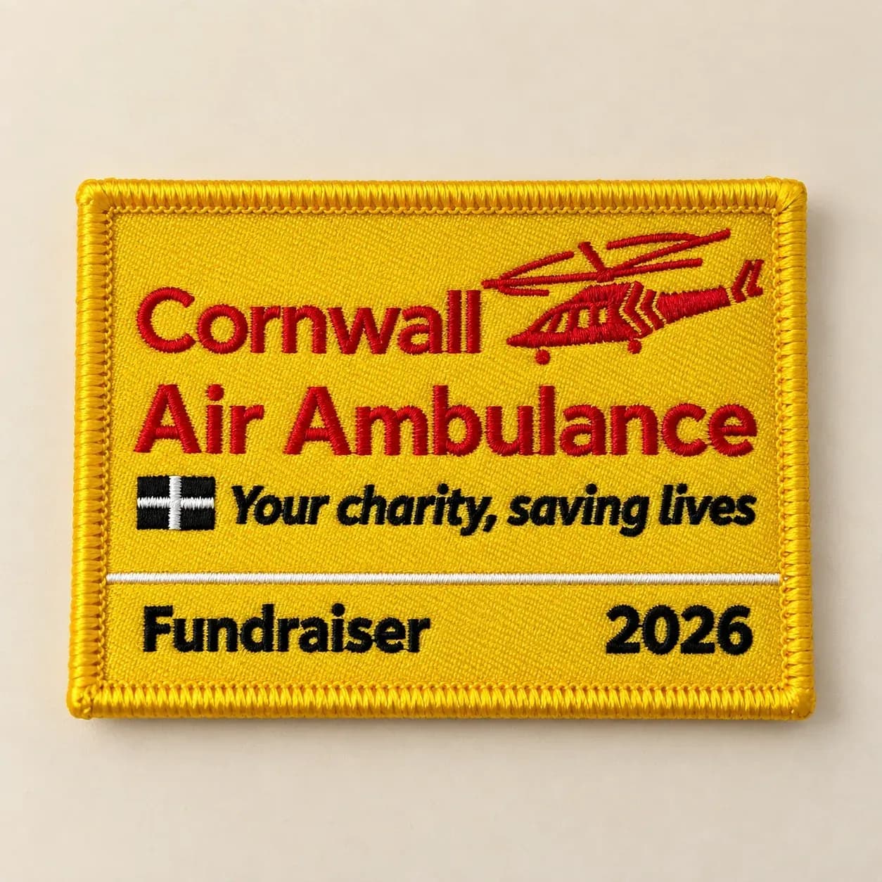Yellow embroidered Cornwall Air Ambulance fundraiser patch with red lettering