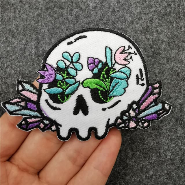 Woven skull patch with flowers and crystals, held in a hand
